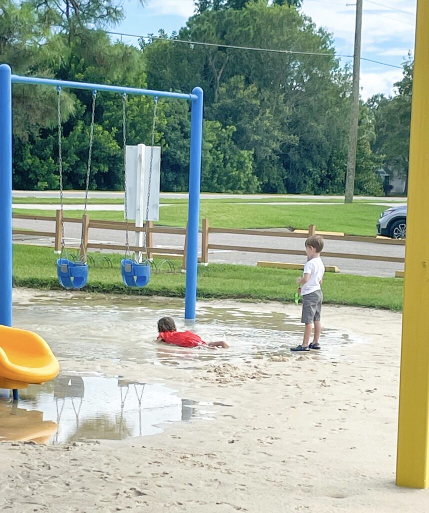 Picture of boy standing in a park watching a girl swim in a puddle