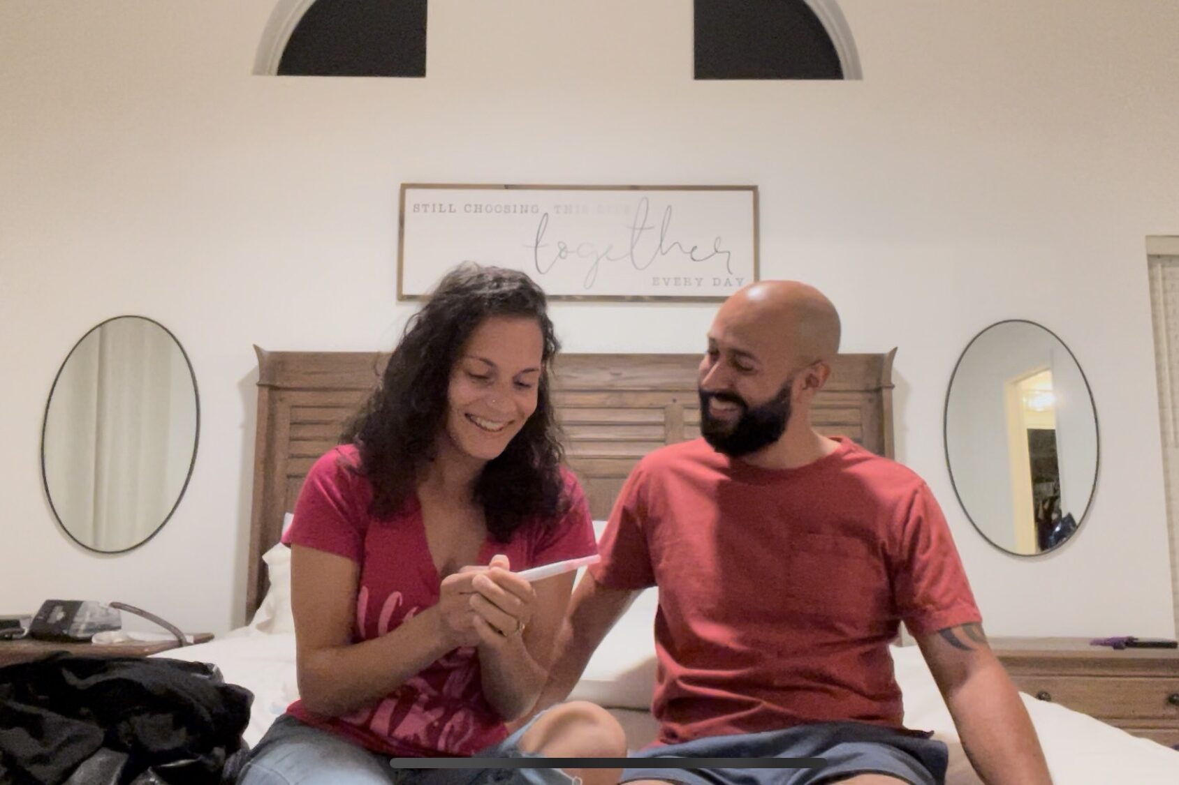 Woman and man on bed smiling looking at a positive pregnancy test